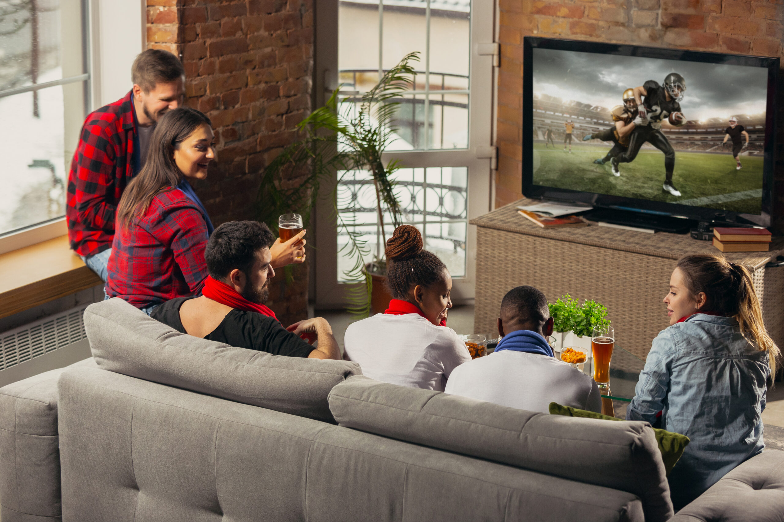Excited group of people watching american football, sport match at home. Multiethnic group of emotional friend, fans cheering for favourite national team, drinking beer. Concept of emotions, support.